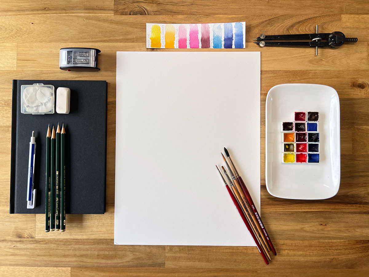 Watercolour pigments, brushes, and cotton paper laid out on the studio table